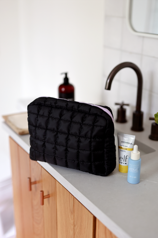 Black quilted cosmetic bag on a countertop with skincare products, stylish and functional for travel.