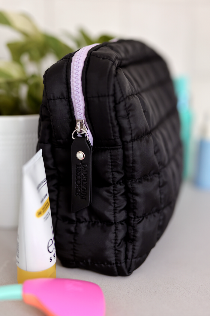 Black quilted cosmetic bag with lavender zipper, perfect for storing beauty essentials.