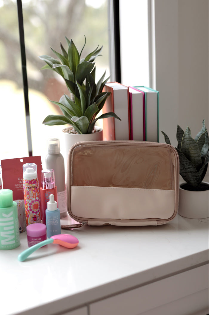 Cosmetic bag on a counter with various items including bottles and a plant in the background.