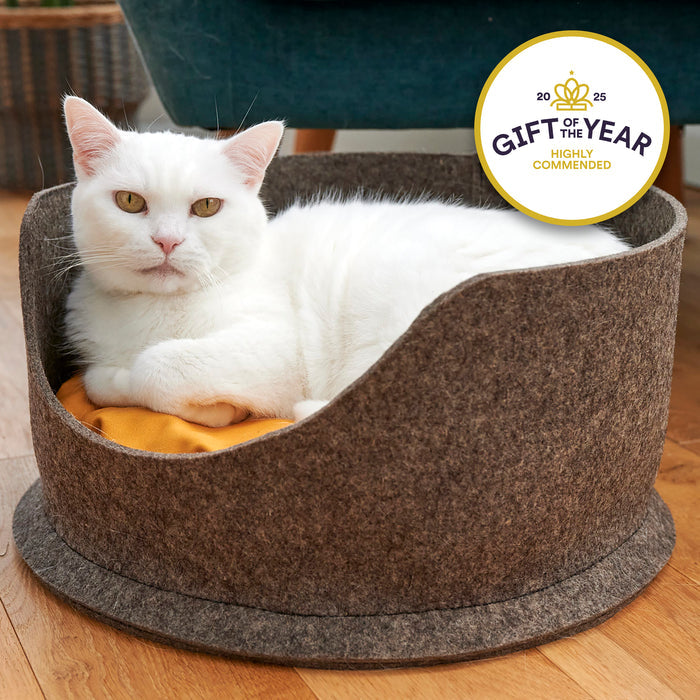 White cat lying in a grey felt pet bed with a 'Gift of the Year' award badge.