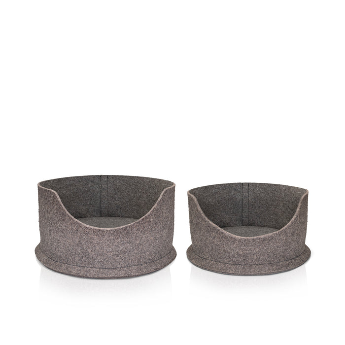 Two Chimney Sheep PetSnug Pet Beds. The small PetSnug is designed to be a cat bed, while the large PetSnug is desigfned to be a large cat or small wool dog bed. These are wool felt cozy beds, made of 100% natural sheep's wool. It is plastic free and pet safe. The pet beds sit upon a white background. It is 3D circular in shape with a dip in the centre to allow easy access for pets.