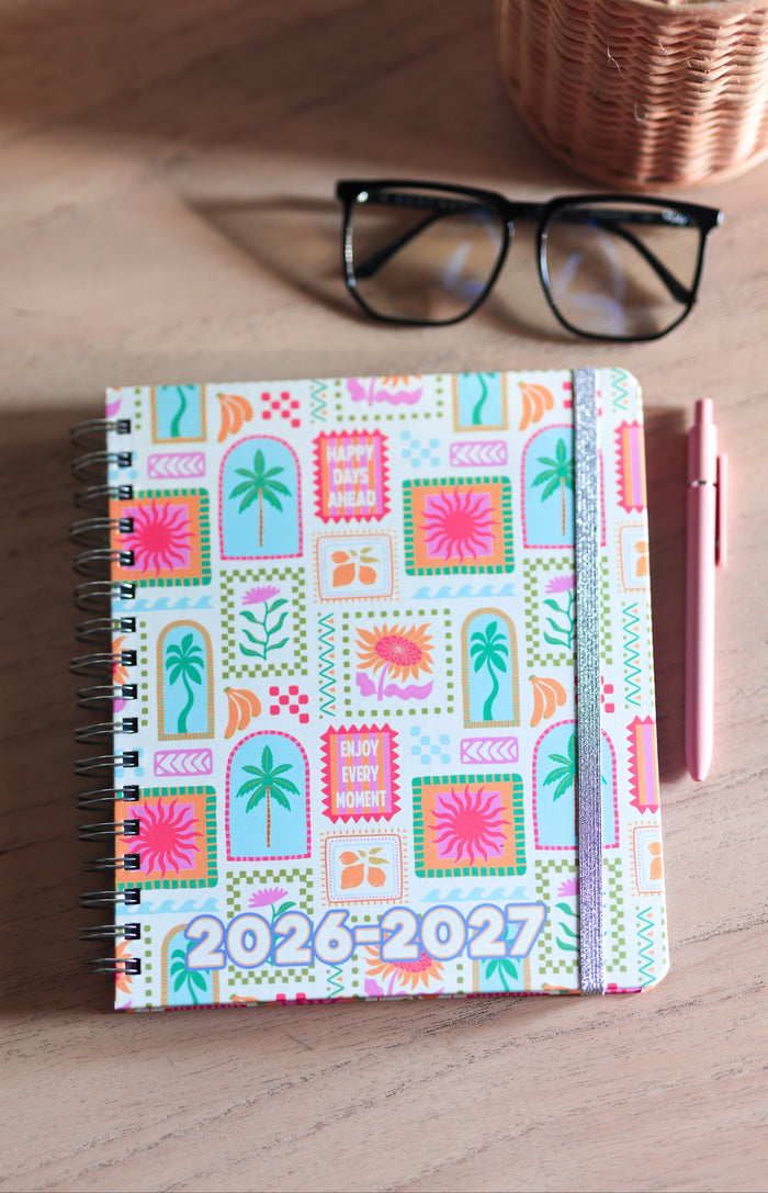 Colorful planner with 2026-2027 text on a wooden surface with glasses and pen.