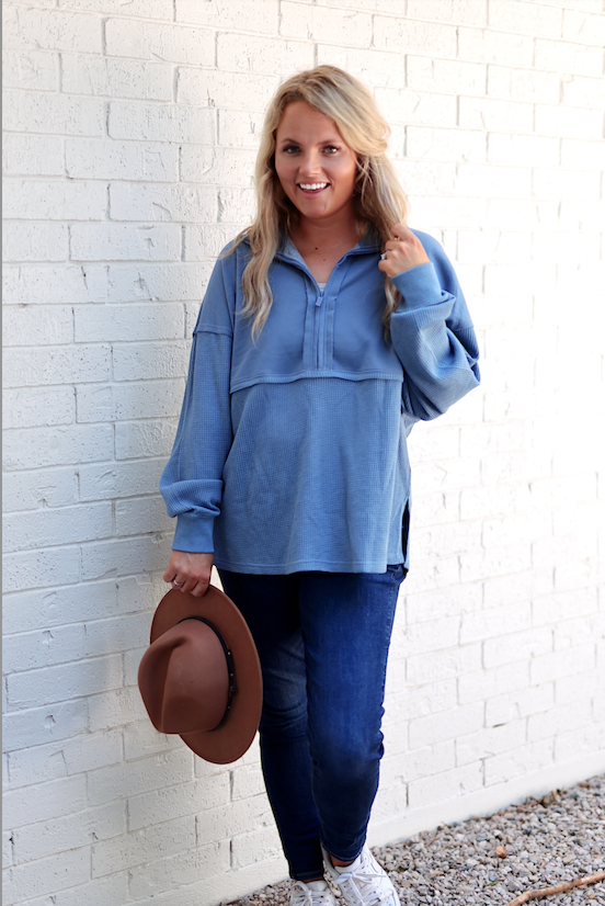 Light blue waffle knit pullover with a half-zip collar, paired with dark jeans and a brown hat.