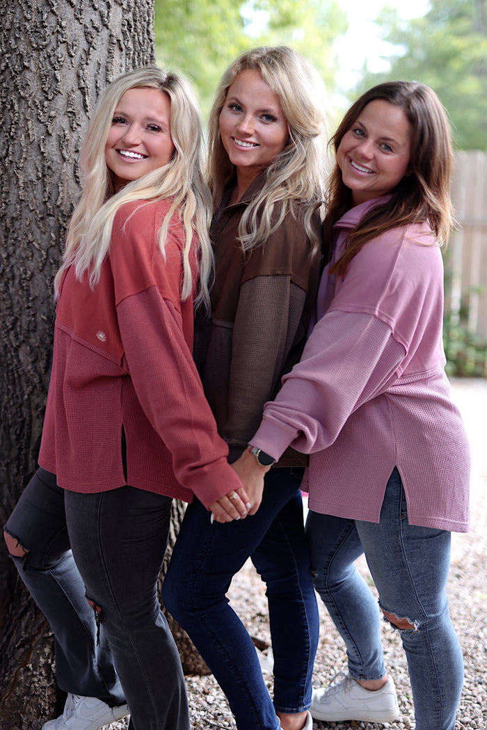 Three women wearing cozy oversized sweaters in pink, rust, and brown, styled with jeans against a tree.