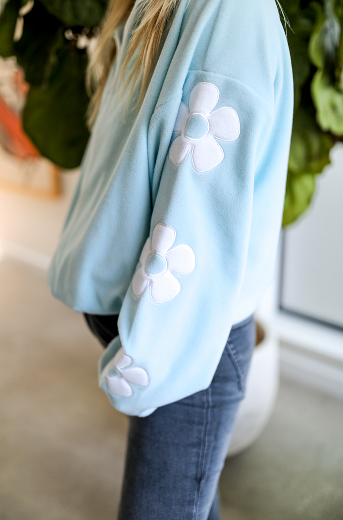 Light blue fleece sweatshirt with white flower appliques on sleeves, perfect for casual wear.