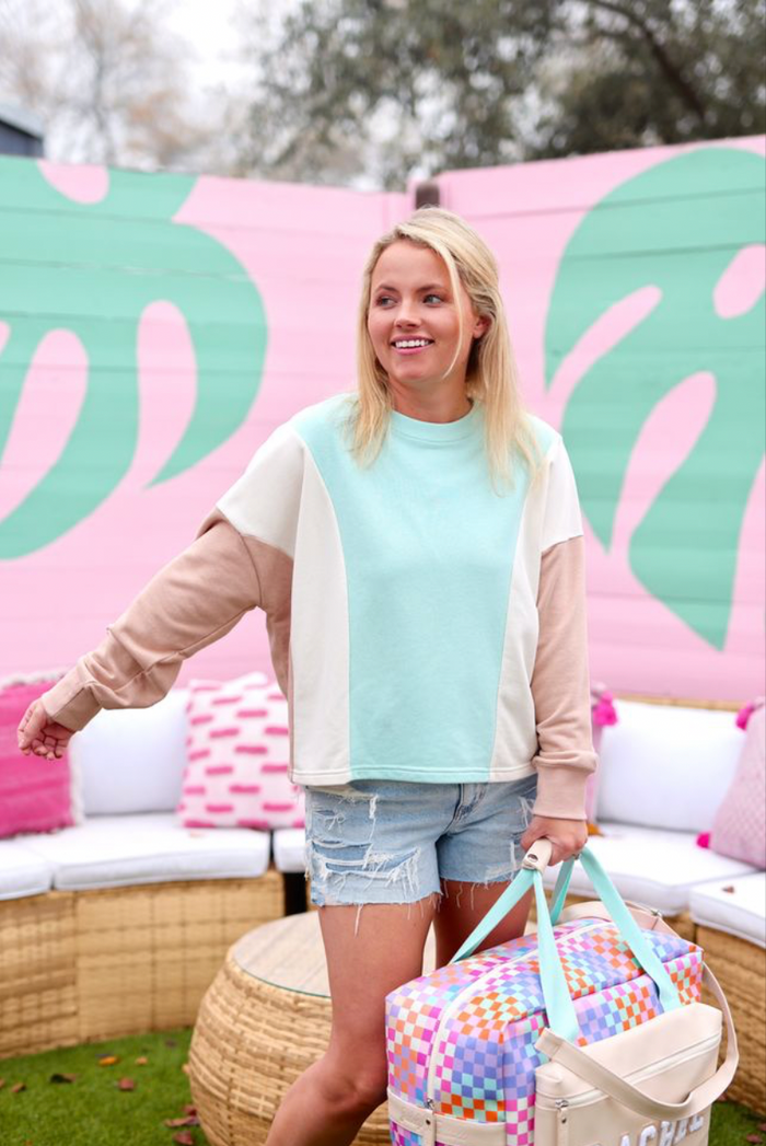 Casual women's sweatshirt in mint green, beige, and cream with distressed denim shorts and a colorful bag.