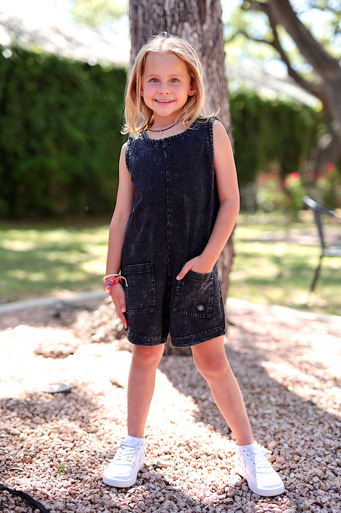 Girls' black denim romper with pockets, perfect for casual outings, paired with stylish white sneakers.
