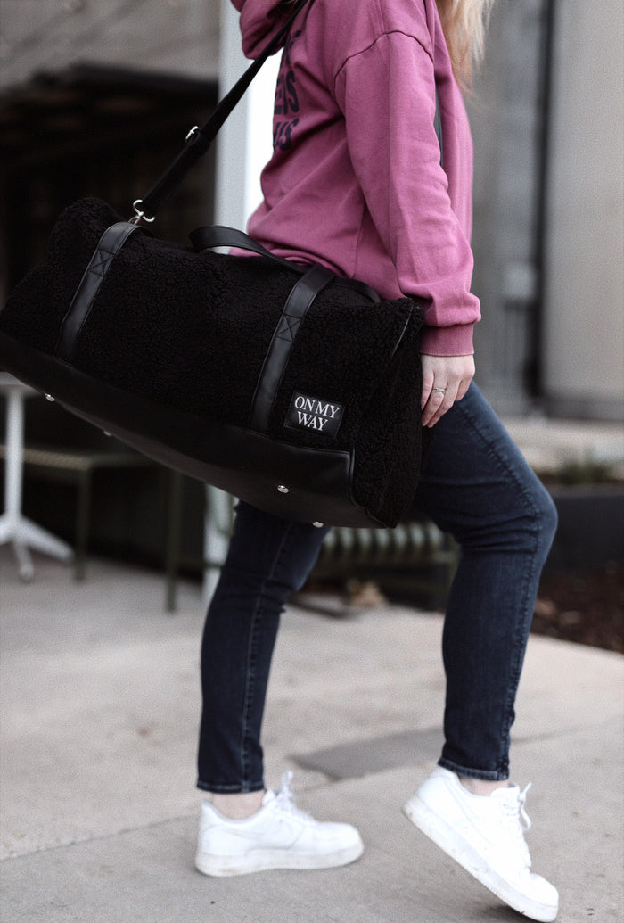 Black faux fur duffel bag with leather accents, featuring 'ON MY WAY' design, perfect for travel or gym.