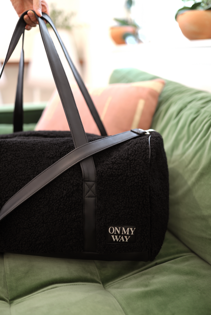 Black plush duffel bag with leather straps, featuring 'ON MY WAY' logo, perfect for travel.