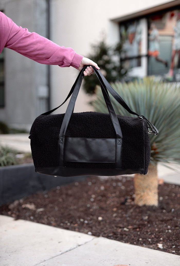 Stylish black duffle bag with faux fur and leather accents, perfect for travel or gym activities.
