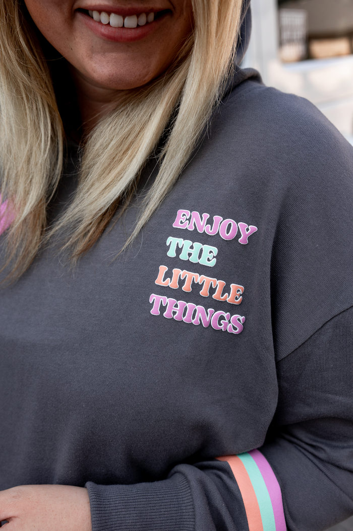 Gray hoodie with 'Enjoy the Little Things' colorful text, featuring striped sleeves and soft material.