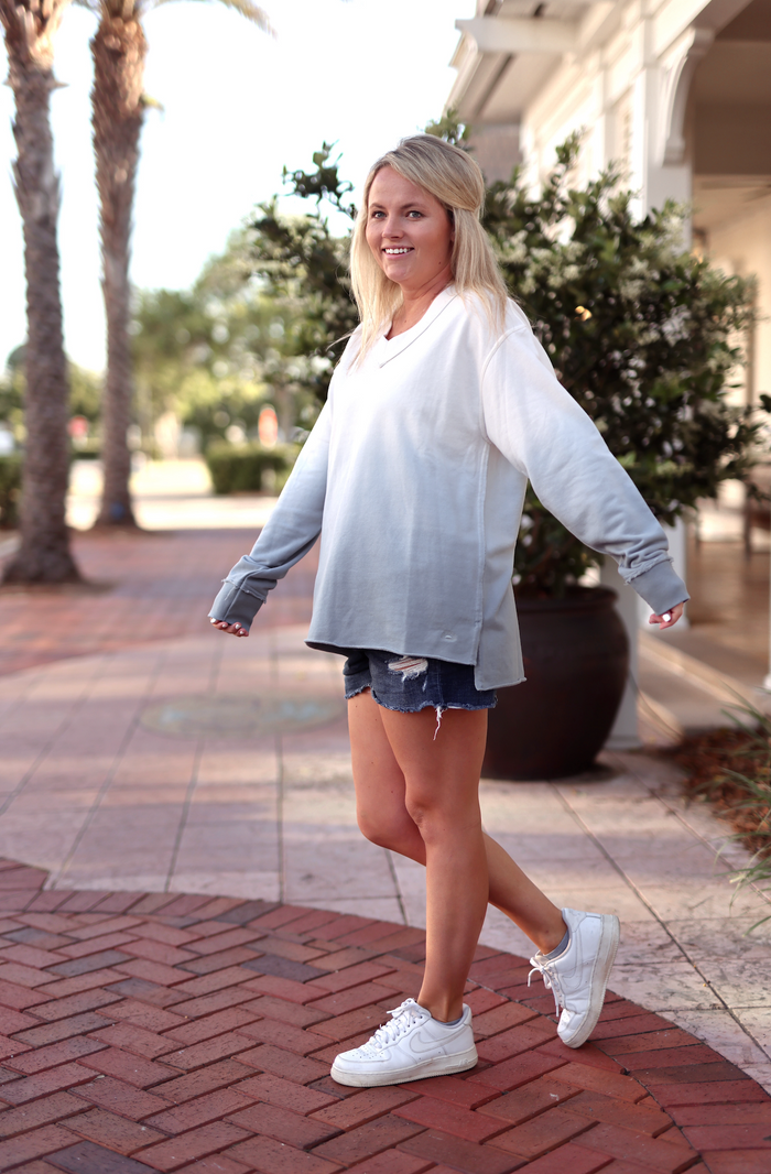 Women's gradient sweatshirt in white to gray, relaxed fit, paired with denim shorts and white sneakers.