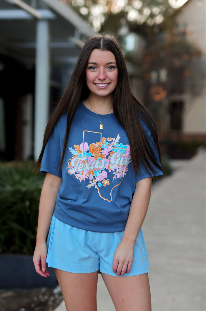 Woman wearing a blue t-shirt with a floral Texas design and matching shorts outdoors.