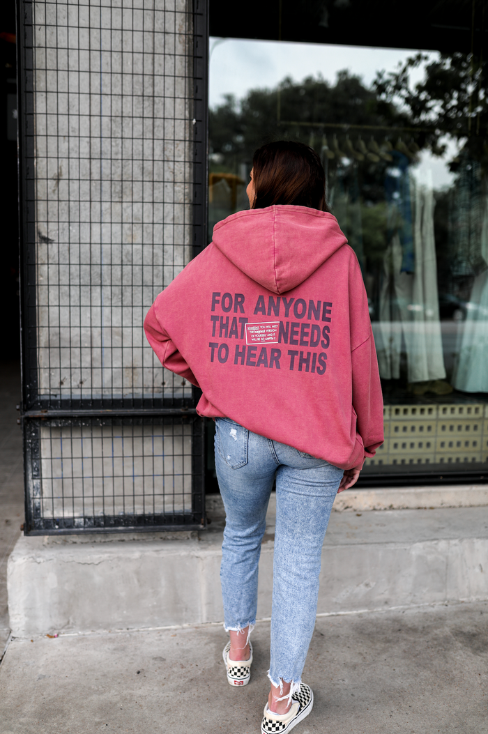 Oversized pink hoodie with text, paired with light blue jeans and checkered slip-on shoes.