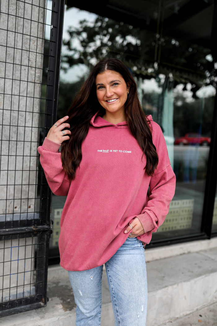 Cozy pink hoodie with 'THE best IS YET TO COME' graphic, perfect for casual or lounge wear.