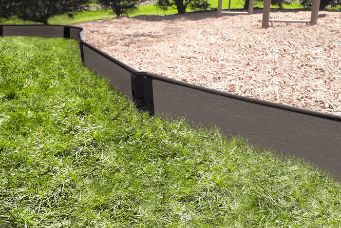 Curved weathered wood playground border with tool-free snap-lock brackets containing wood chip safety surfacing between grass and play area