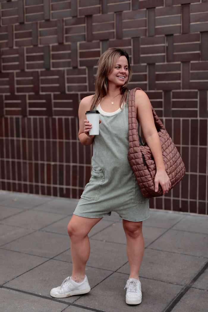 Woman in a light green sleeveless dress with pockets, holding a coffee, wearing a brown quilted bag.