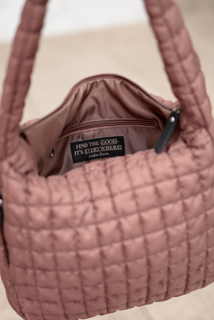 Inside view of a quilted blush pink handbag with a zip pocket and brand logo.