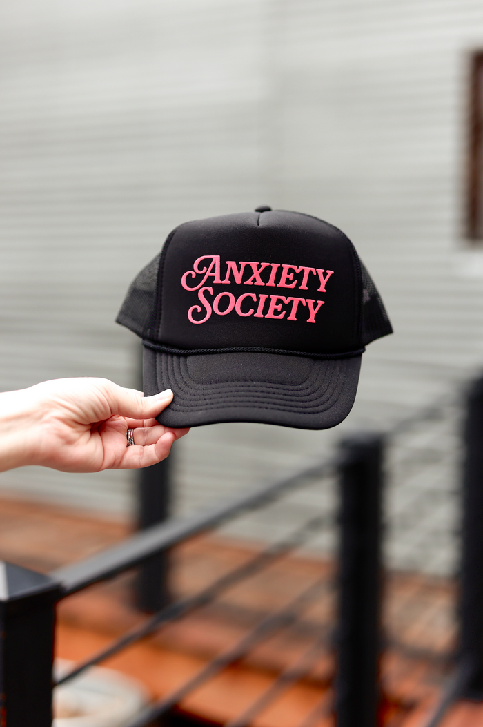 Black trucker hat with pink 'Anxiety Society' logo, perfect for casual wear and promoting mental health awareness.