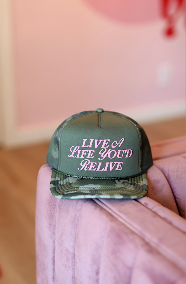 Green camo snapback hat with 'LIVE A LIFE YOU'D RELIVE' in pink lettering.