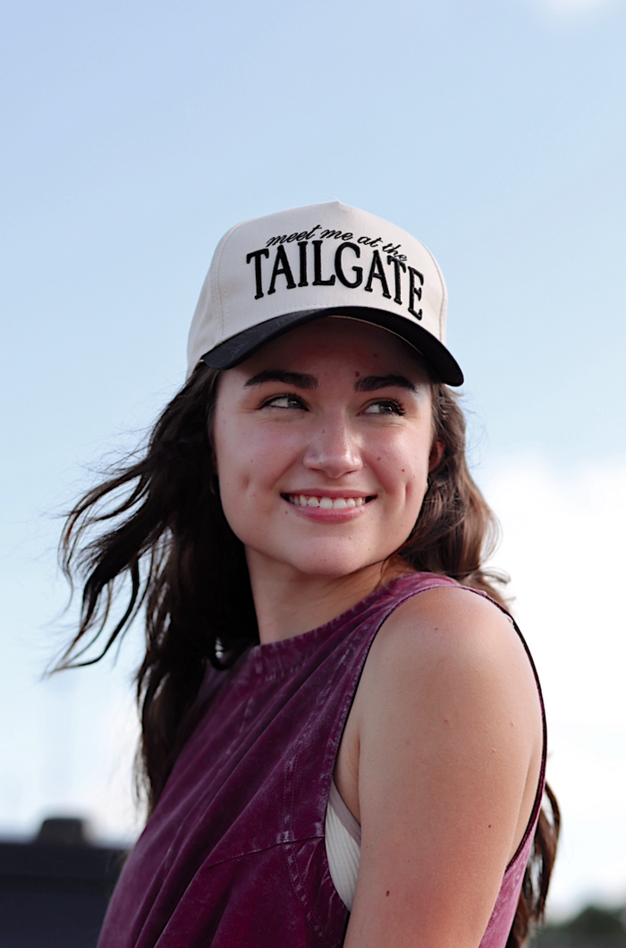 Stylish woman wearing a burgundy sleeveless dress and beige cap with 'TAILGATE' text.