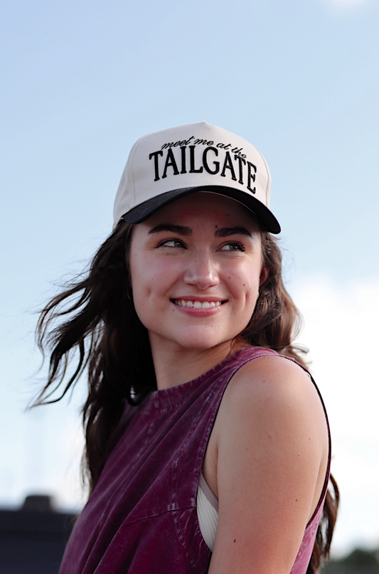 Stylish woman wearing a burgundy sleeveless dress and beige cap with 'TAILGATE' text.