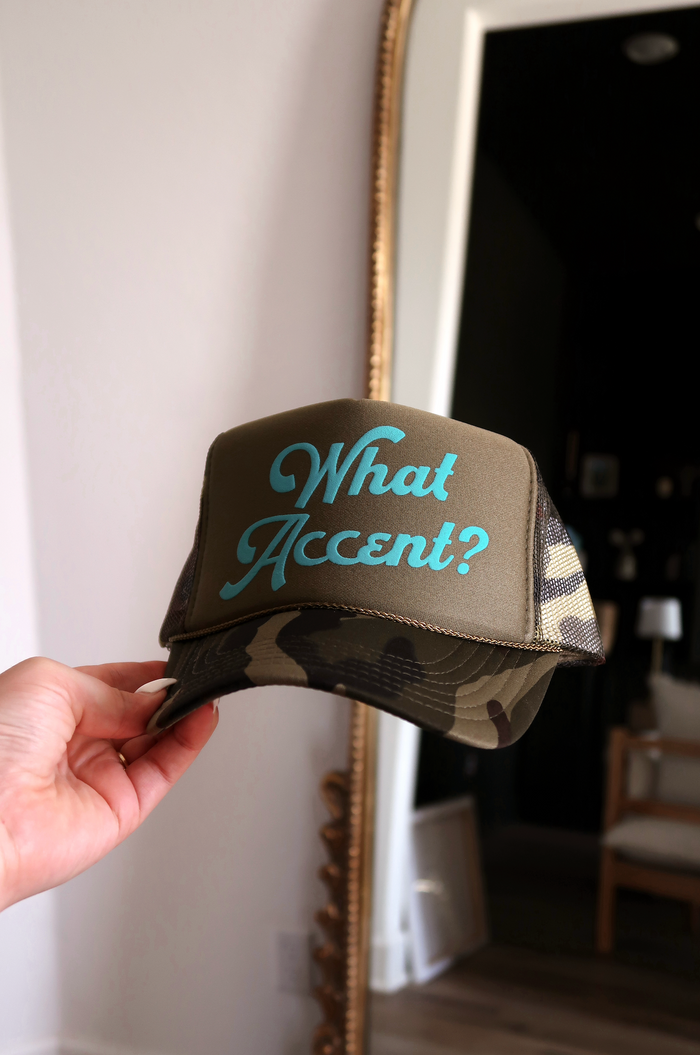 Brown camo trucker hat with turquoise 'What Accent?' text, perfect for outdoor style.