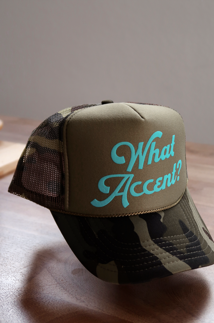 Camo trucker hat featuring aqua text design 'What Accent?' on olive green fabric.