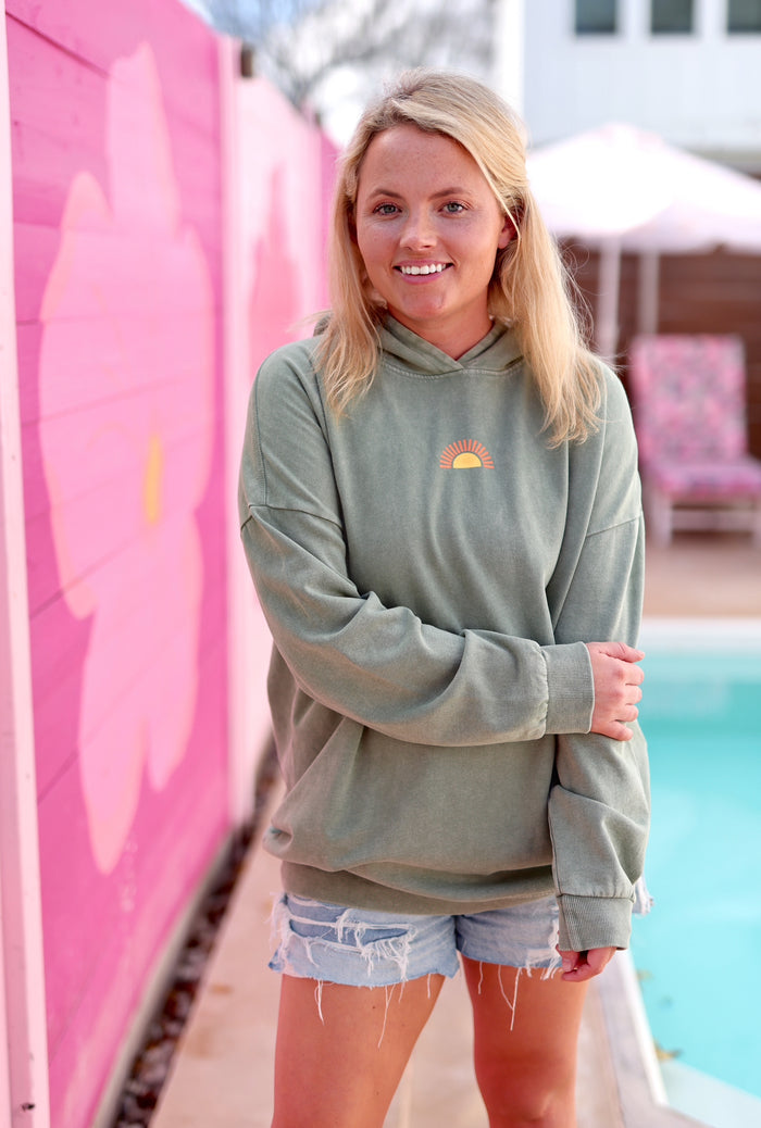 Light green oversized hoodie with sun graphic, paired with distressed denim shorts by the pool.
