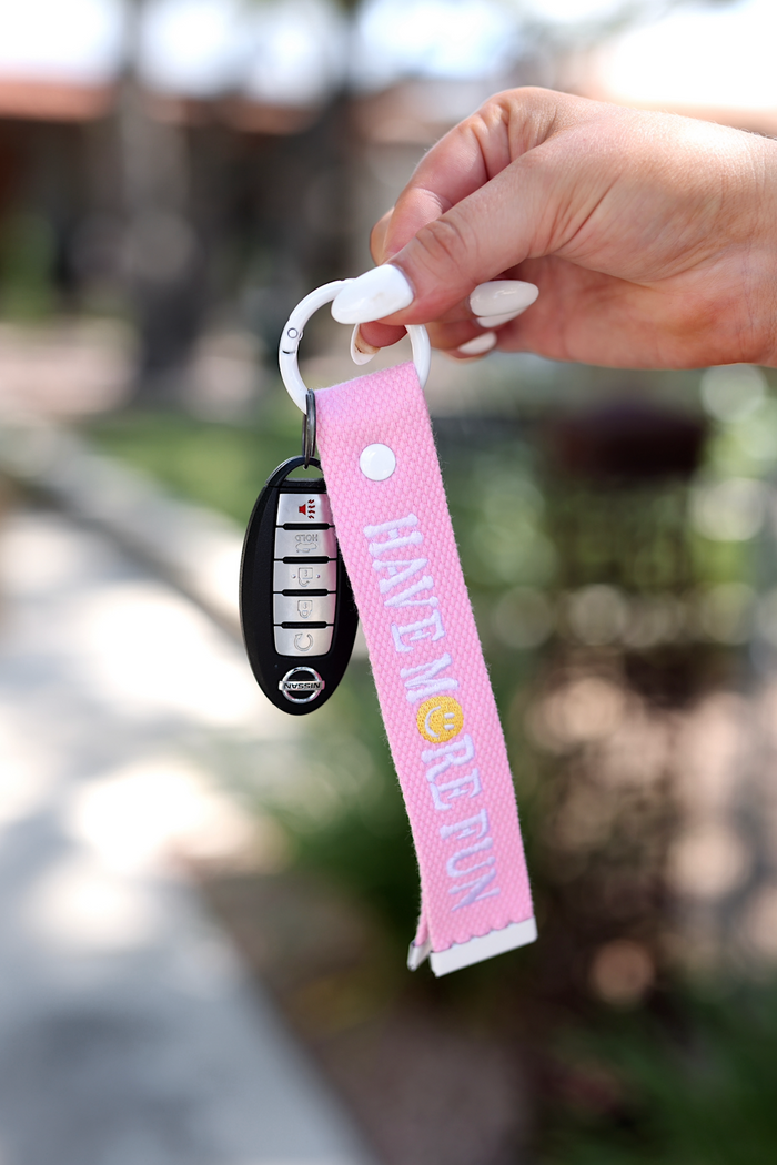 Pink fabric keychain with 'HAVE MORE FUN' text, showcasing a Nissan car key attached.