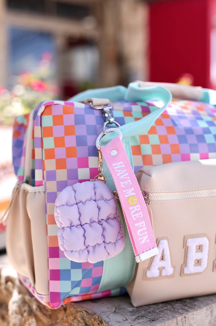 Colorful checkered backpack with pastel accents and fluffy keychain, perfect for stylish travel.