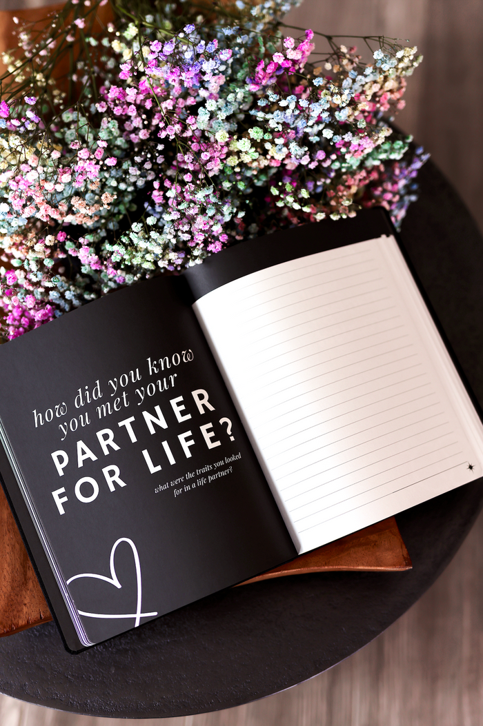 Black journal with quotes about finding a life partner, surrounded by colorful flowers on a table.