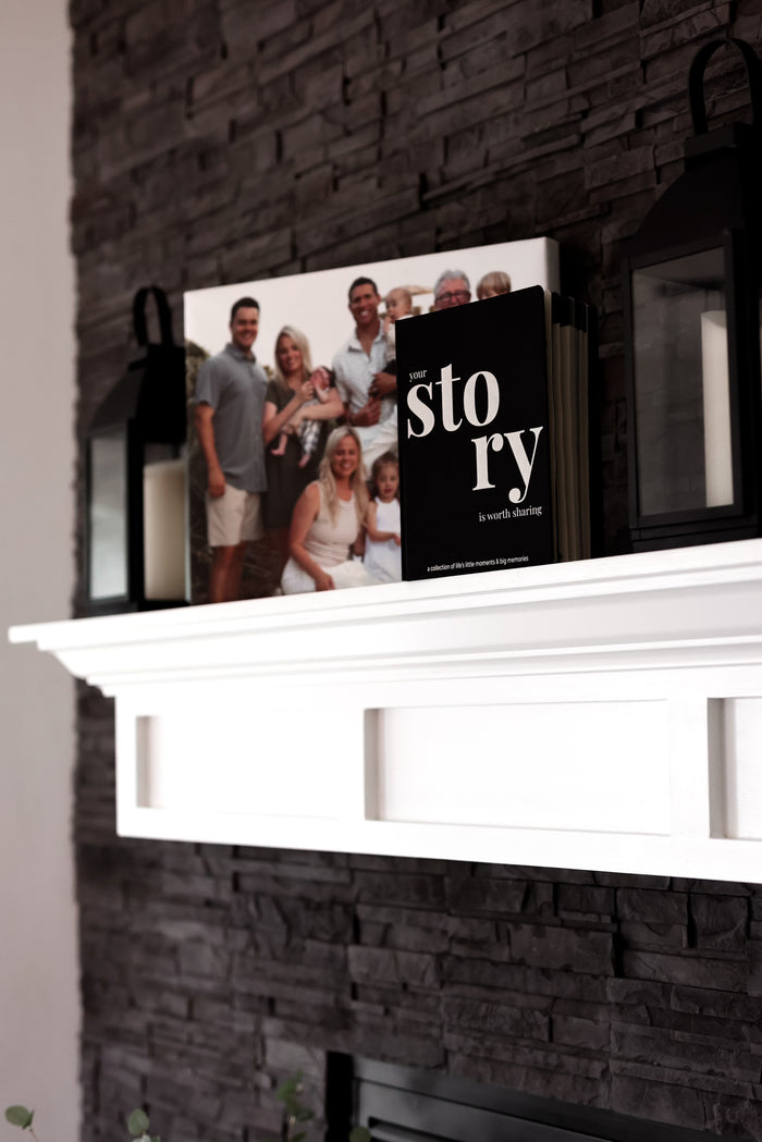 Black hardcover book 'Your Story' displayed on a white mantel with family photo backdrop.