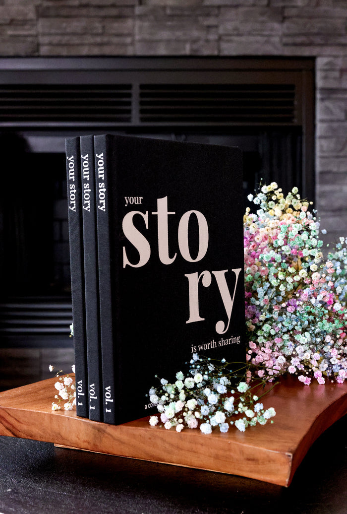 Set of three black storybooks with floral accents on a wooden display, designed for sharing personal stories.